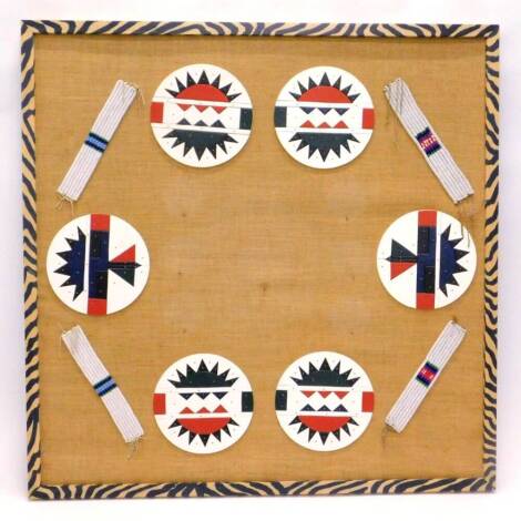 A collection of African tribal art, to include six roundels, each with polychrome geometric decoration, and four narrow bead work bracelets, the frame, painted to simulate Zebra skin, 127cm x 127cm.