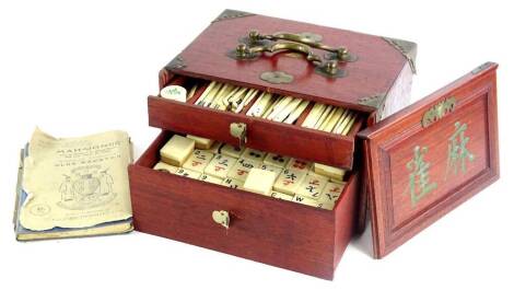 An oriental bone mahjong set, in hardwood case with brass fittings and a book on mahjong.