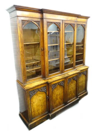 A Victorian oak and walnut veneered breakfront bookcase, in Gothic style, with the moulded cornice above four glazed doors, with arched astragals, enclosing adjustable shelves, the base with four doors, each with pierced Gothic roundel's, on plinth base, 