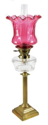 A late 19thC oil lamp, with clear chimney, fluted cranberry glass shade and glass reservoir, on a brass column and stepped foot, 74cm H.