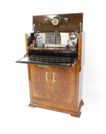 An Art Deco walnut and burr walnut cocktail cabinet, the rise and fall front opening to reveal a mirror backed fitted interior, with lighting, cocktail shaker, lemon squeezer and pins, above two doors, opening to reveal a single shelf, raised on stepped f