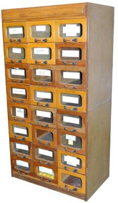 An early 20thC shop cabinet, set with an arrangement of eight banks of three drawers, each with glass fronts, flanked by plain stiles, 153cm H, 82cm W, 49cm D.