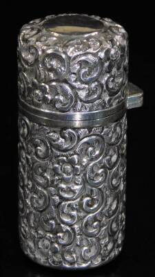 An Edwardian silver perfume bottle, of cylindrical form, heavily repousse decorated with scrolls, with hinged lid and glass stopper, Chester 1903, 10cm H, 3½oz all in.