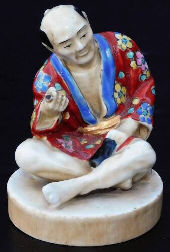 An early 20th Japanese pottery figure, of a gentleman seated in flowing robes, florally decorated predominately in yellow, blue and red, on a circular foot, impressed mark JAPAN beneath, 9cm H.