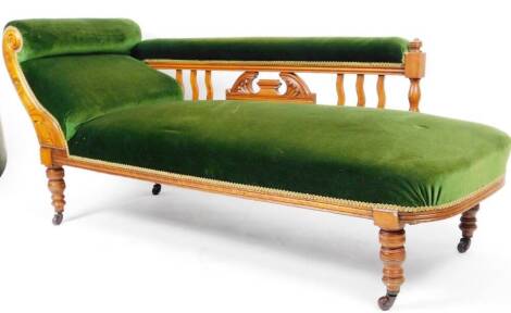 An early 20thC walnut chaise longue, in green material, with scroll arm, plain back with a carved scroll design on turned legs terminating in castors, 78cm H, 180cm W, 62cm D.