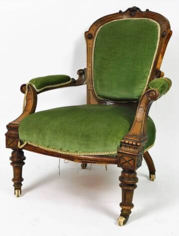 A late Victorian walnut occasional chair, with heavily carved back, overstuffed back, arms and seat in green material, with inverted front carved arm supports and turned front legs terminating in castors, 104cm H.