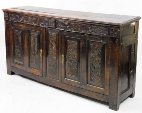 A heavily carved English oak side cabinet or court cupboard, the rectangular plank top raised above a carved frieze set with scrolls, above two panelled cupboard doors, on block stiles, part 18thC, 89cm H, 170cm W, 44cm D.