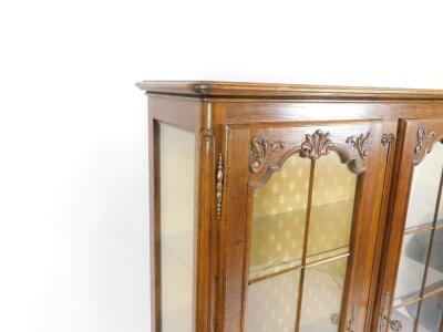 An 18thC style oak display cabinet, carved with rococo scrolls and leaves, having two glazed doors opening to reveal two glass shelves, raised on cabriole legs, 158cm H, 115cm W, 37cm D. - 2