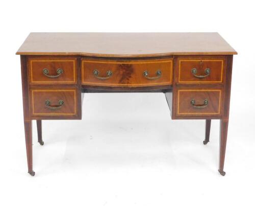 An Edwardian mahogany and satinwood crossbanded bow front dressing table, converted to a desk, with a bow front drawer flanked by four single drawers, raised on tapering square legs, capped on castors, 77cm H, 122cm W, 38cm D.