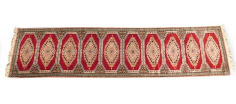 A Tekke runner, decorated with ten medallions, within a floral geometric border, against a red ground, 341cm x 79cm.