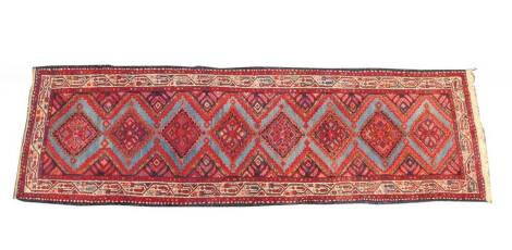 A Turkish runner, decorated with eight geometric motifs, within a geometric and figural border, against a blue and red ground, 286cm x 88cm.