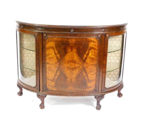 An early 20thC mahogany bow front sideboard, the central door opening to reveal two shelves, flanked by two glazed doors, opening to reveal two glass shelves, fabric backed, raised on cabriole legs and ball and claw feet, 100cm H, 136.5cm W, 53cm D.