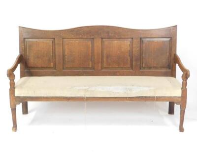 A 19thC oak settle, with a four panelled back, scrolling arms, with over stuffed seat, raised on turned legs, 183cm W.