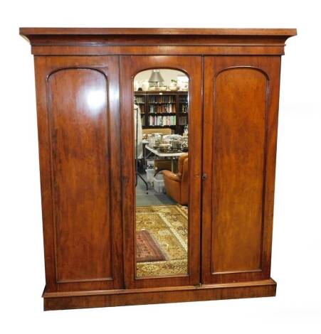 A Victorian plum pudding mahogany compactum wardrobe, the outswept pediment over three doors, the central door inset with glass, opening to reveal four slides above two short over two long drawers, flanked to the right by a hanging rail and further drawer