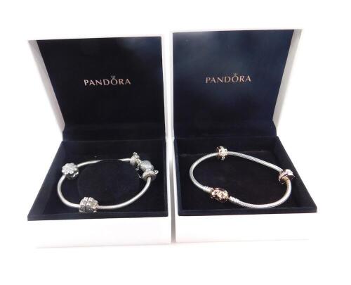 Two Pandora bracelets, one with a yellow metal heart shaped charm and two paste set cylindrical charms, the other with a heart shaped charm, two four section heart shaped charms, and a pair of wheel form cuffs, both boxed.