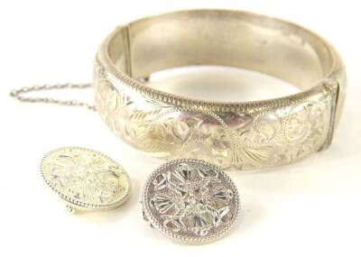 Three items of silver jewellery, comprising a Victorian hinged bangle, with scroll motifs, and two matching silver circular brooches, with urns, baskets and shells, makers stamp R.S, 2cm W, 44.4g all in.