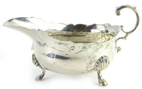 A George V silver sauce boat, with a shaped border, scroll cast handle and three cabriole shaped legs, headed by shells, London 1929, 6¼oz.