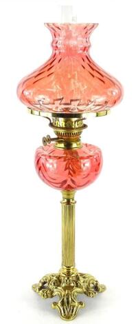 A Victorian style brass oil lamp, with cranberry tinted shade and reservoir, on column base, 65cm H.