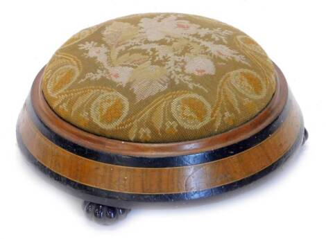 A Victorian ebonised and walnut circular foot stool, with woolwork seat, on lobed black ceramic feet, 31cm dia.