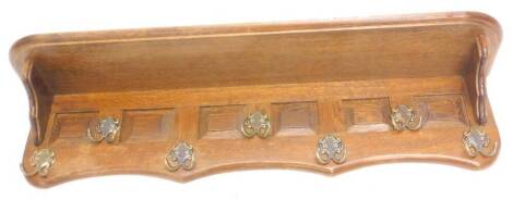 A Continental oak wall mounted coat rack, with panelled front and six gilt metal hooks below a shelf, 100cm W.