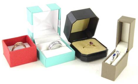 Four modern dress rings, to include a 9ct gold garnet dress ring, a silver blue and white stone half hoop eternity ring, a silver CZ dress ring, and a silver rose coloured multi stone ring, boxed. (4)