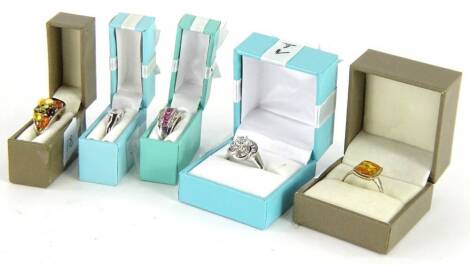 Five modern silver dress rings, comprising a silver and amber dress ring, a silver and CZ floral cluster ring, silver and amber multi stone ring, CZ solitaire ring, and a three row white and pink stone dress ring, boxed. (5)