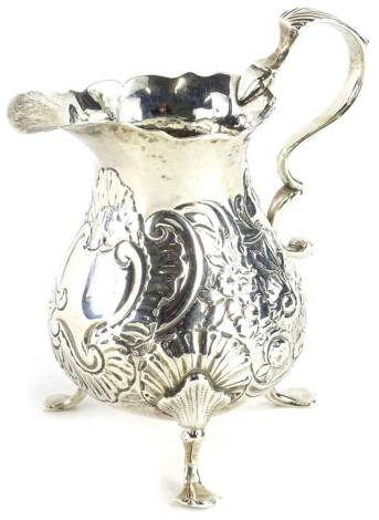 An early 19thC silver inverted baluster cream jug, embossed with scrolls, flowers, leaves, etc., on three feet, marks indistinct, 3oz.