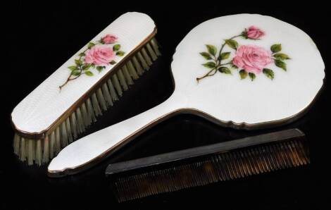 A silver backed comb, London 1961 and an enamel backed hand mirror and matching clothes brush, both with rose bud decoration. (3)