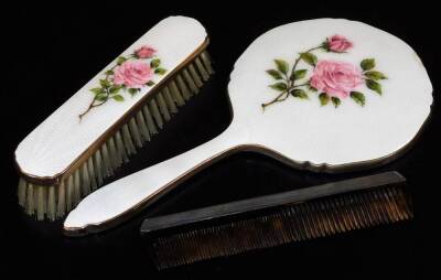 A silver backed comb, London 1961 and an enamel backed hand mirror and matching clothes brush, both with rose bud decoration. (3)