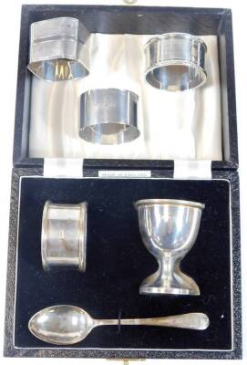 A silver christening set, comprising egg cup, spoon and napkin ring, in presentation case, Birmingham 1959/60, 1.52oz and three silver napkin rings, 2.86oz., total weight 4.38oz.