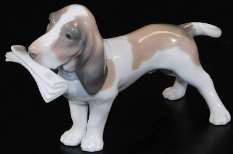 A Lladro figure of a Bassett hound, with newspaper to the mouth, printed marks beneath, 19cm W.