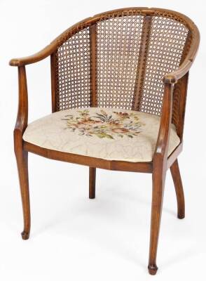 An Edwardian mahogany and bergere tub chair, with overstuffed seat in petit point floral material, on turned front and sabre back legs, 76cm H.