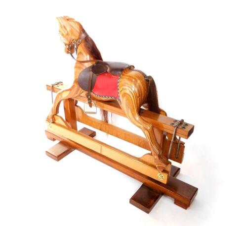 A marquetry and pine rocking horse, with red and brown leather saddle, and metal stirrups, 102cm H, 179cm W.