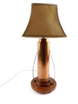 An Art Deco copper table lamp, of hammered double cylindrical form, with scroll arms, raised on a stepped oak circular base, on bun feet, with shade, 61cm H.