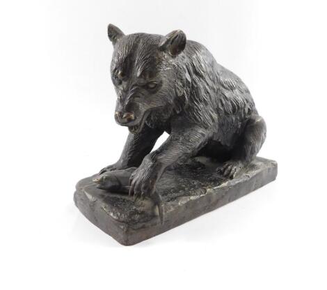 A bronze figure of a bear, modelled seated with it's front paw resting on a fish, raised on a naturalistic rectangular base, unsigned, 28cm W, 12.5cm D, 21cm H.