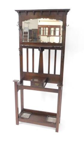 A Victorian oak hall stand, the outswept pedimented back over a bevelled glass mirror and shaped shelves, flanked by hanging hooks, over a small glove box, flanked by two stick recesses, above an under tier with drip trays, raised on square straight suppo