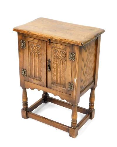 An Elizabethan style oak cupboard, with two panelled doors carved with Gothic tracery, raised on turned legs, united by stretchers, 68cm H, 50.5cm W, 32cm D.