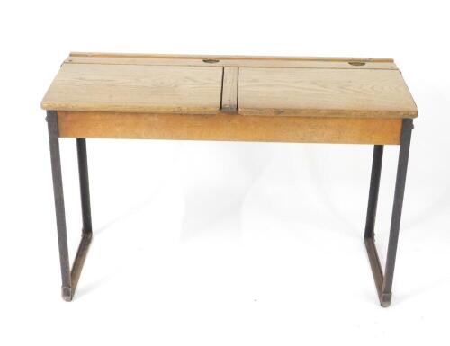 An early 20thC oak and cast iron framed child's double desk, with one long pen recess, two ink well recesses and two lift up lids, raised on straight metal supports, 61cm H, 92cm W, 38cm D.