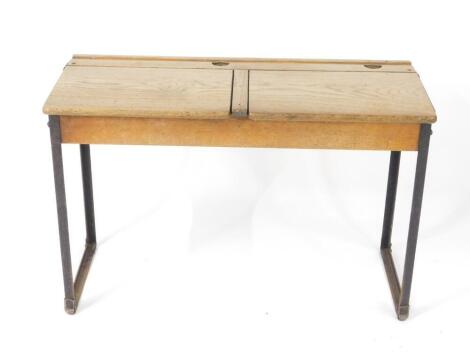 An early 20thC oak and cast iron framed child's double desk, with one long pen recess, two ink well recesses and two lift up lids, raised on straight metal supports, 61cm H, 92cm W, 38cm D.