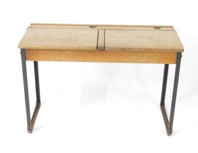 An early 20thC oak and cast iron framed child's double desk, with one long pen recess, two ink well recesses and two lift up lids, raised on straight metal supports, 61cm H, 92cm W, 38cm D.