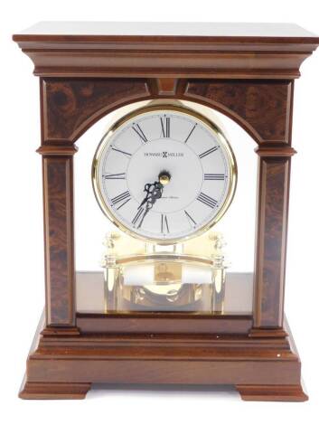 A Howard Miller Statesboro cherry and burr veneered mantel clock, circular white dial, bearing Roman numerals, Quartz movement, the brass case of cylindrical form, raised on a four pillar support, with pendulum below, in a wooden and four sided glazed cas