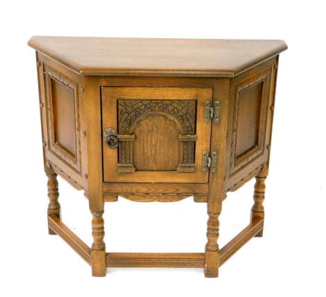 An Old Charm oak Elizabethan style side cupboard, of demi hexagonal form, with a single panelled door carved with an arch, raised on turned legs united by stretchers, 71cm H, 80.5cm W, 32cm D.