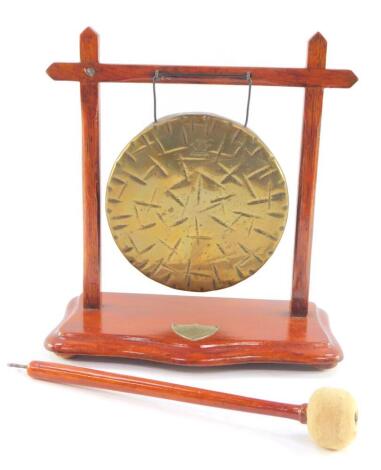 A Burmese brass table gong, in a wooden frame, on a serpentine base, with clanger, 25cm W.