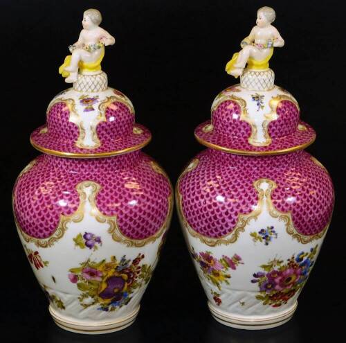 A pair of Meissen porcelain vases and covers, each exquisitely decorated with flowers, with domed circular lids surmounted by cherub and garland finials, each main body decorated with feathered pink and purple panelling, with further handpainted flowers o