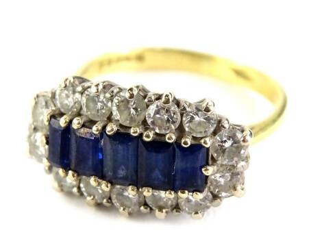 An 18ct gold sapphire and diamond dress ring, with five central rectangular cut sapphires, each in claw setting, surrounded by fourteen round brilliant cut diamonds, on a raised claw head, ring size N½, 5.4g all in.