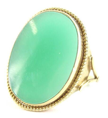 A 9ct gold and jade dress ring, the oval jade in rub over setting, 1.8cm x 2.5cm, with a reeded design border, with V split shoulders, ring size N, 5.3g all in. (AF)