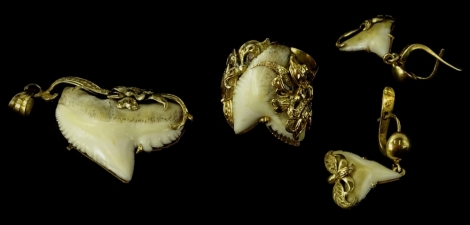 A group of shark's tooth set jewellery, comprising a dress ring, set with central tooth, with floral design scroll borders and flowers, yellow metal, unmarked, a pair of matching drop earrings and a matching pendant. (3) Provenance - believed to have been