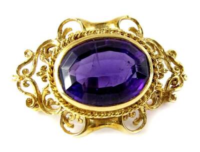 A Victorian style amethyst brooch, with central oval faceted amethyst, in scroll design frame, yellow metal, partial marks for London 1969, 4cm wide, 11g all in.