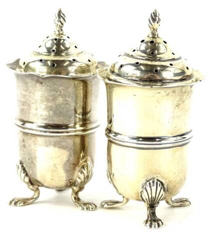 A pair of Edwardian silver pepper pots, each with a flame finial a cylindrical body with central moulded band on three shell capped feet, Chester 1909, 2½oz.