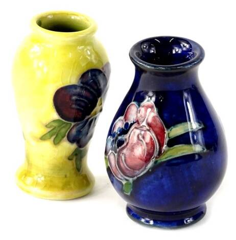 A Moorcroft miniature pottery baluster shaped vase, decorated with pansies on a dark blue ground, 5.5cm H, and a similar yellow ground vase, 5cm H. (2)